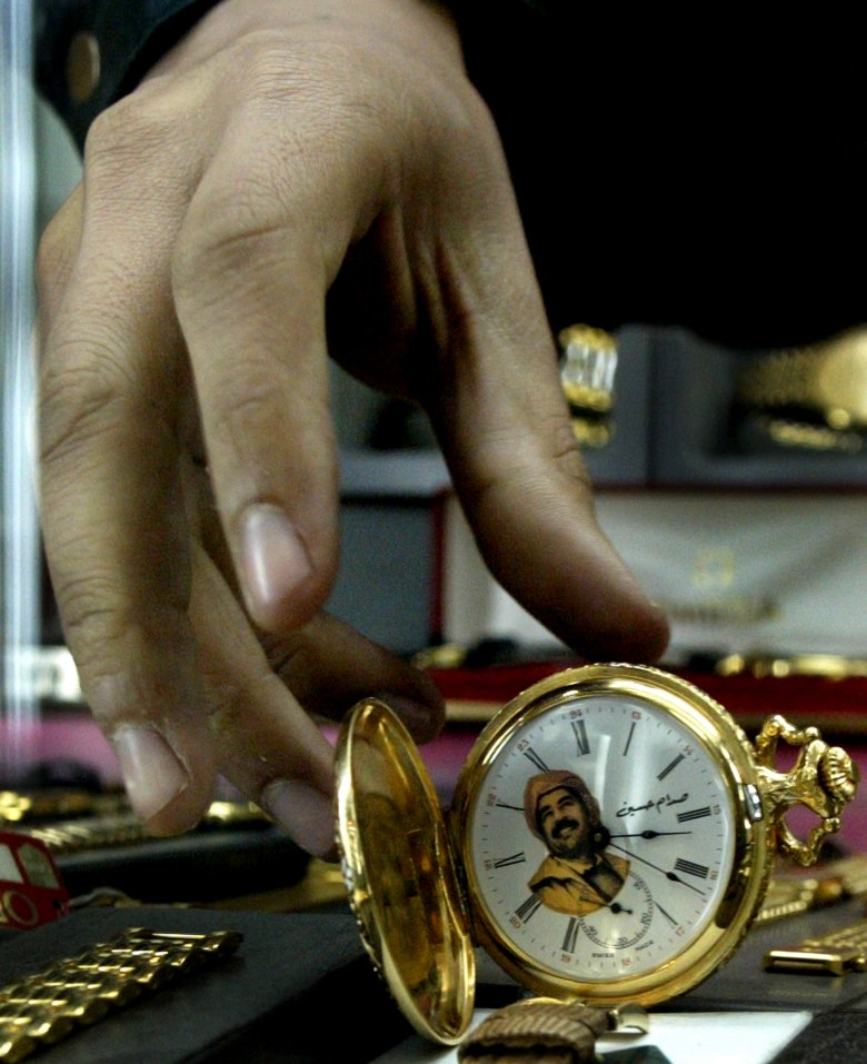 Sprzedawca wyciąga rękę po zegarek z wizerunkiem Saddama na targowisku w centrum Bagdadu