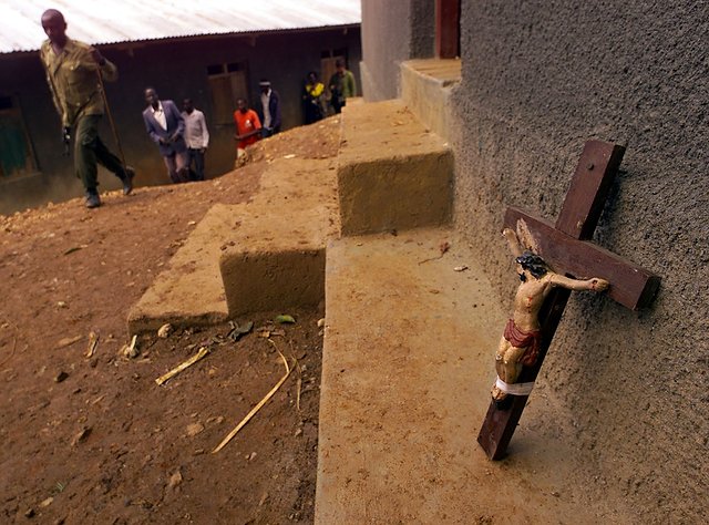 Mieszkańcy Kanungu i krzyż oparty o budynek sąsiadujący z kościołem, w którym spalono żywcem kilkaset osób.
