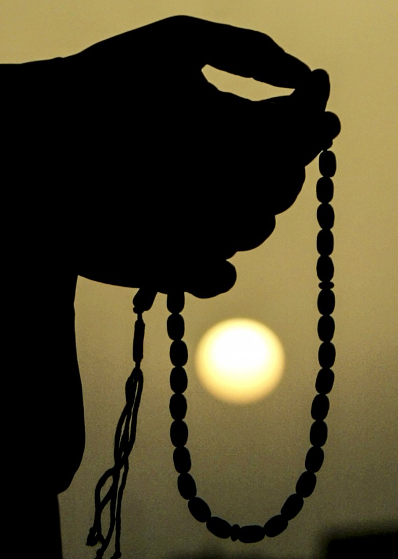 Mężczyzna przesuwający paciorki modlitewnego sznura o zachodzie słońca w mieście Samala.