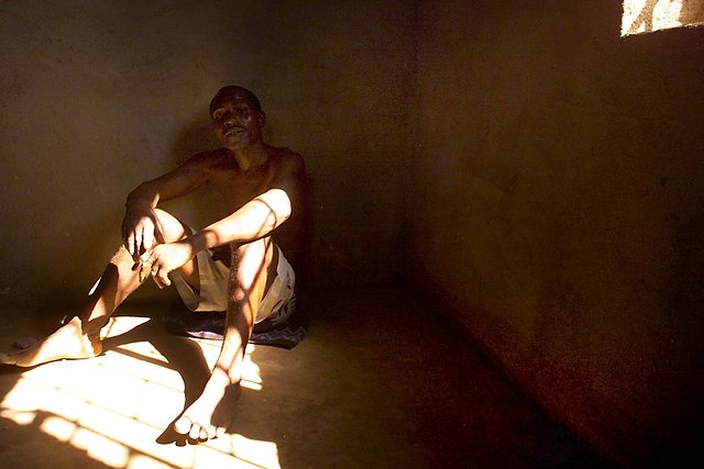 Wyczerpany więzień siedzi na podłodze domu, pod którego podłogą ukryto ponad 150 ciał zamordowanych członków sekty.