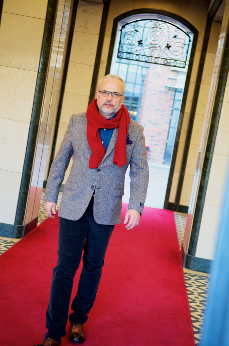 Bogdan ma na sobie: jeansową koszulę marki Brooks Brothers -  cena: 525 zł; wełnianą marynarkę marki Brooks Brothers - cena: 1875; kaszmirowy szalik marki Brooks Brothers - cena: 1404 zł oraz sztruksowe spodnie marki Jacob Cohen - cena: 1188 zł.